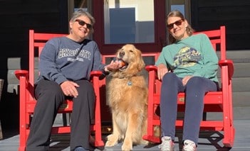 Peggy, Tucker the dog, and Mary Wendling sitting on rocking chairs